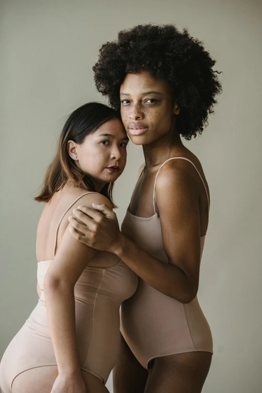 two women in beige one - piece and one wearing short pants standing side by side