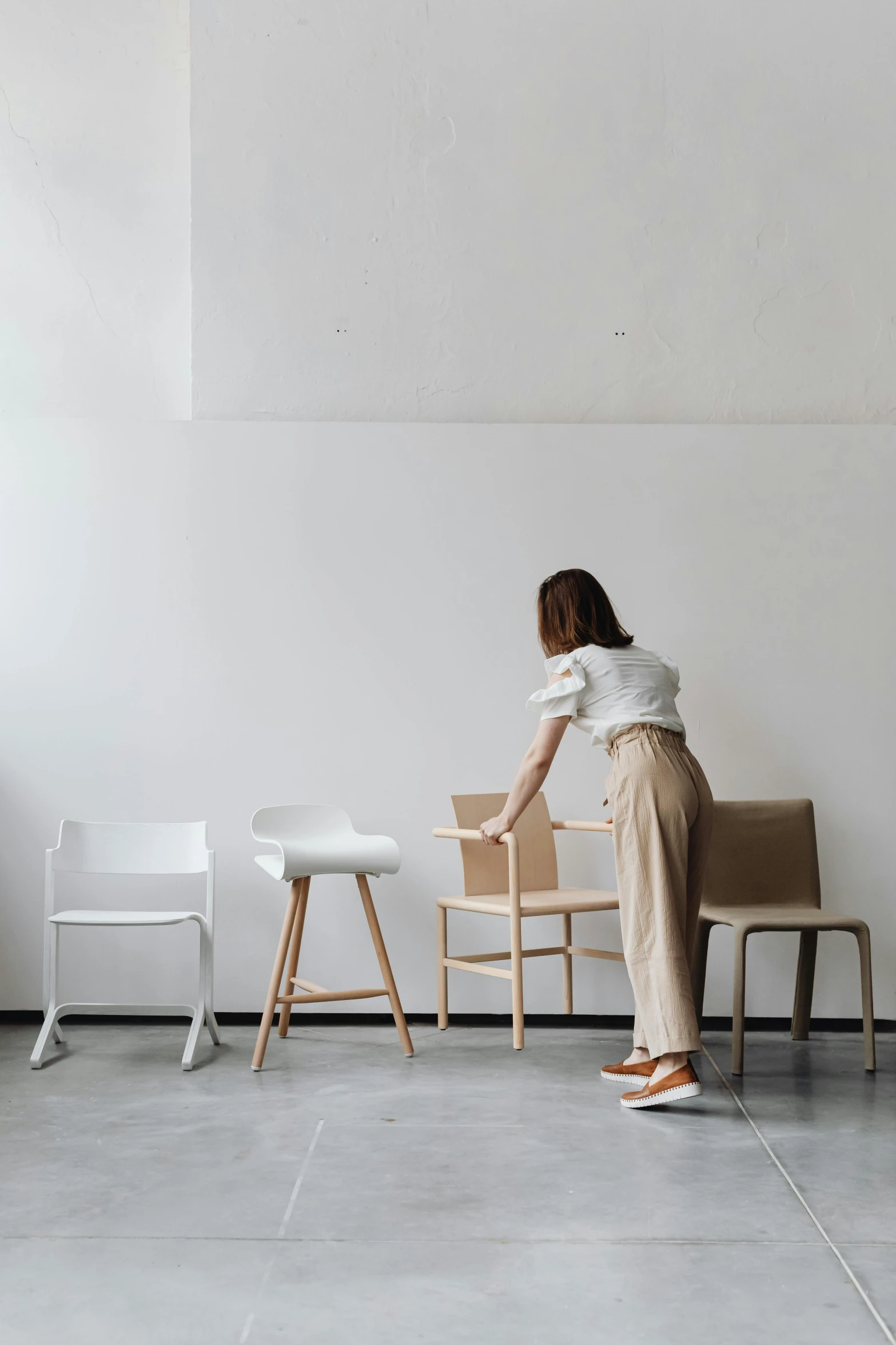 a woman in white shirt and tan pants leaning on the edge of a chair