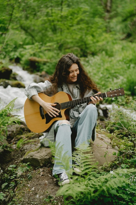 a man with long hair playing guitar in a forest