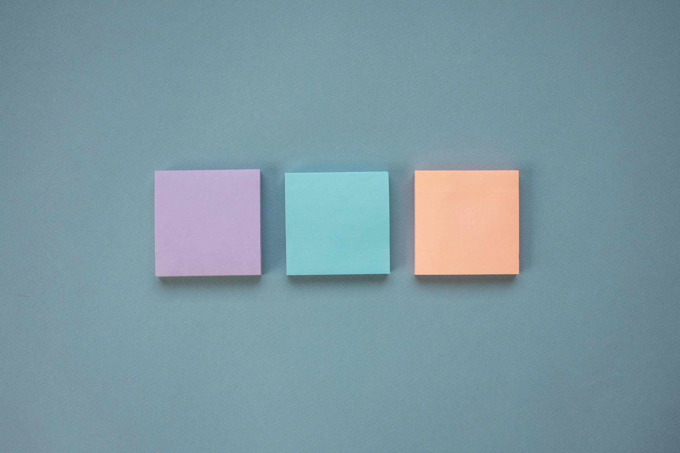 three squares of colored sticky paper arranged on a blue surface