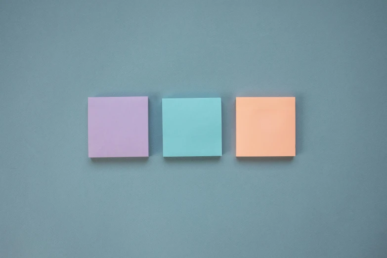 three squares of colored sticky paper arranged on a blue surface