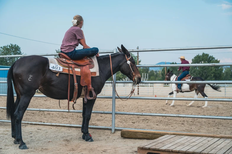 woman sitting on saddle of horse in pen while people watch