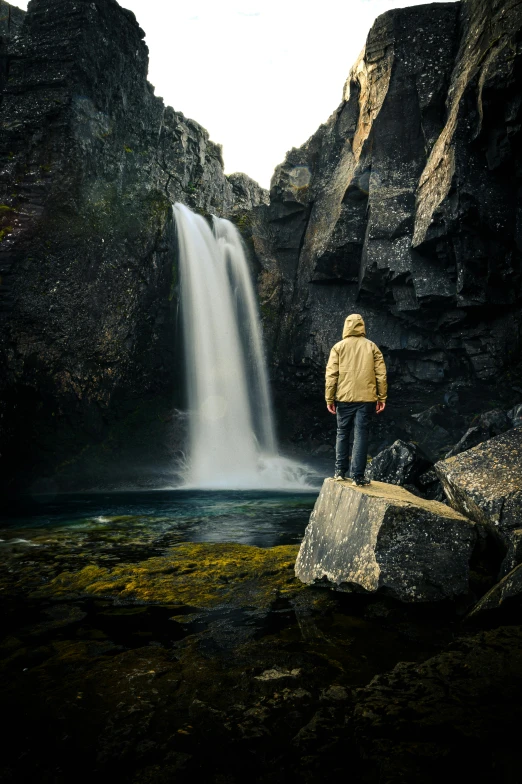 the man stands by the waterfall and looks out