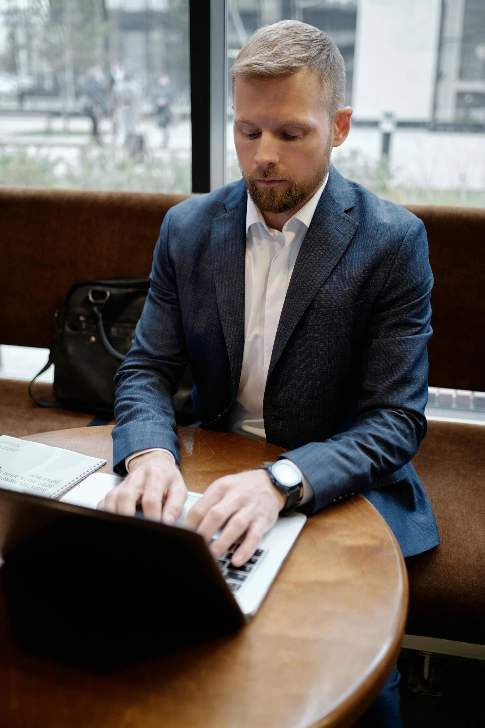 man in black jacket typing on laptop at wooden desk