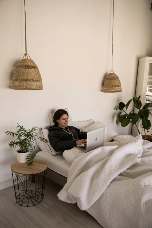 a woman sitting on a bed while using a laptop