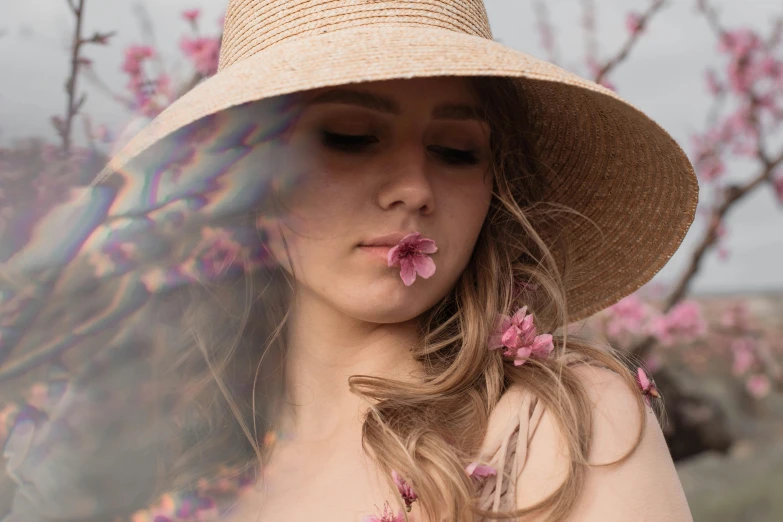 the young woman is wearing a straw hat and holding pink flowers