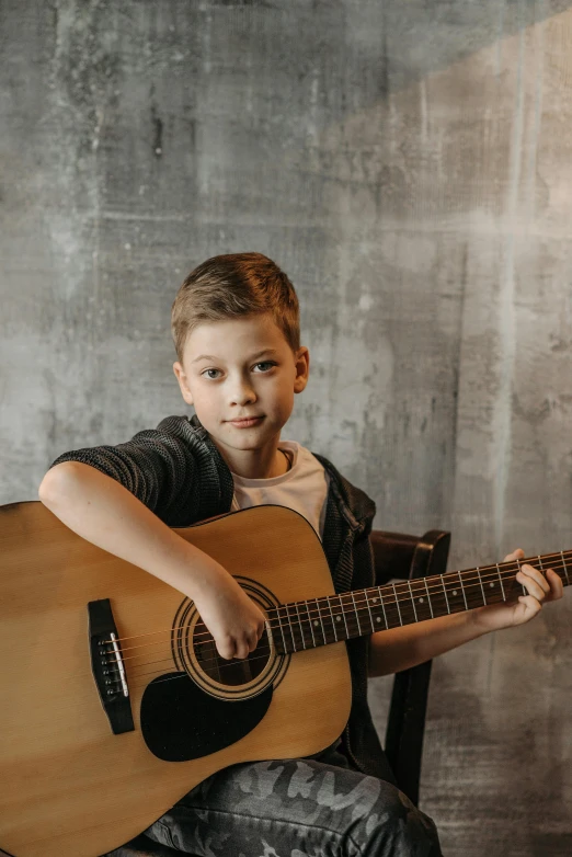 a boy in black jacket holding up an acoustic guitar