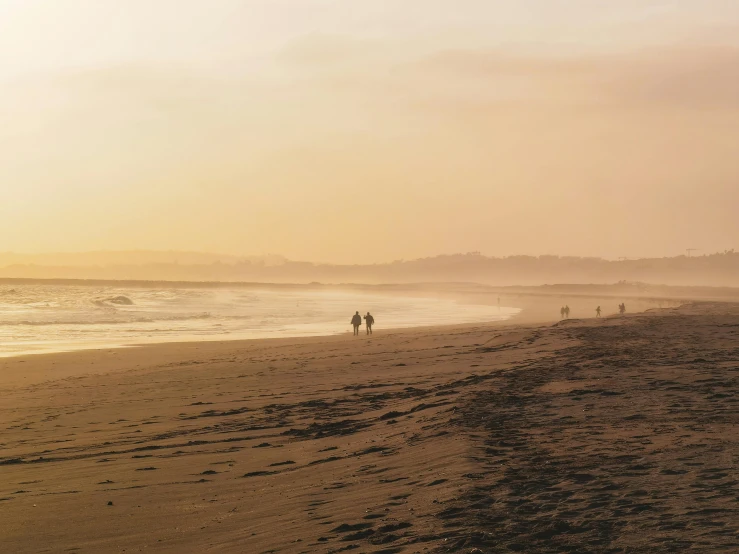 people are walking along the beach at sunset