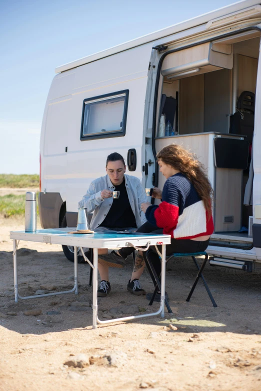 a man and woman sitting outside their camper on the ground