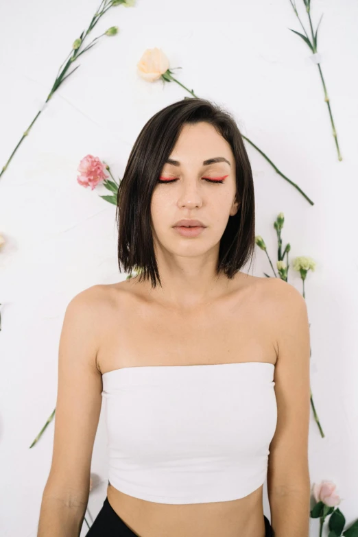 young woman in white top sitting by flower wall