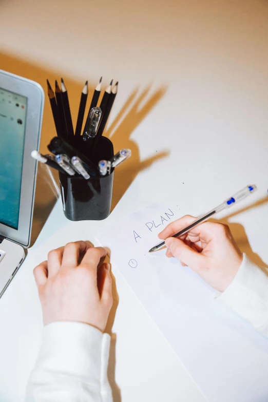 a person using their laptop at a desk with a notepad and pencil