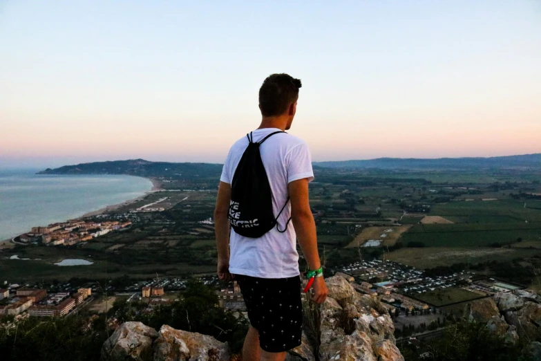 man with backpack looking out over the ocean from atop a rock