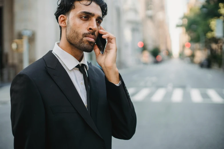 man in black suit on cell phone standing at the side of a city street