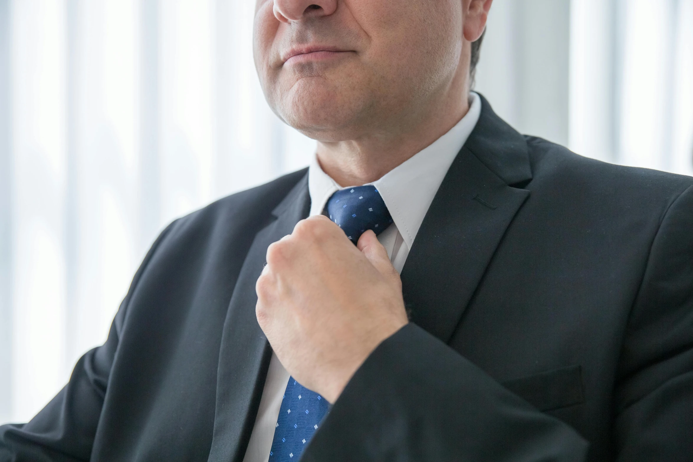 a man adjusting his tie while in front of a window