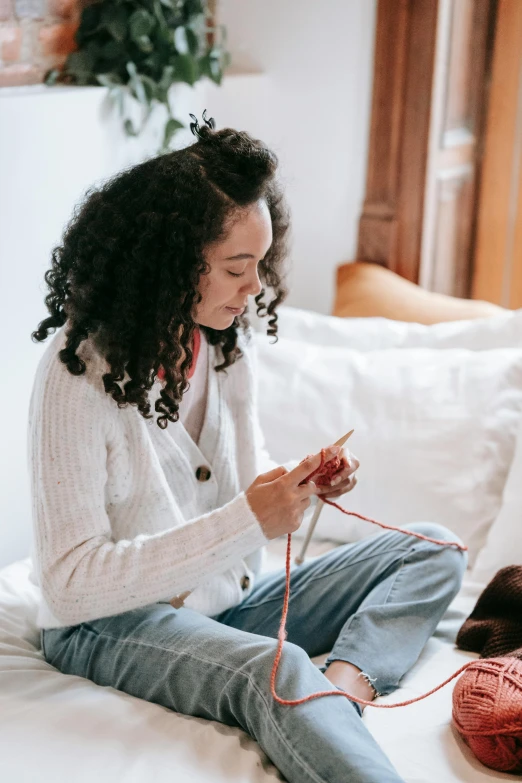 the woman is knitting and sitting on the bed