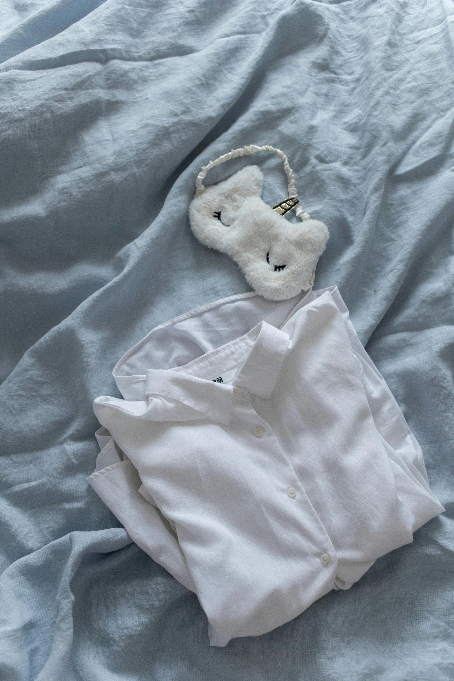 white shirt sitting on a bed with a teddy bear attached to the pillow