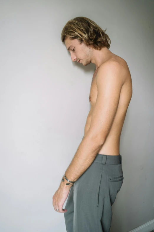 a shirtless young man standing next to a wall