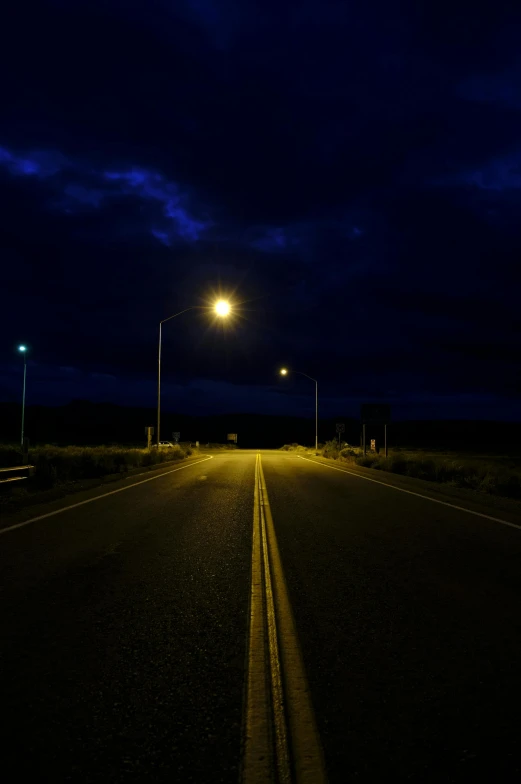 an empty road with three poles on either side and two lights on the other