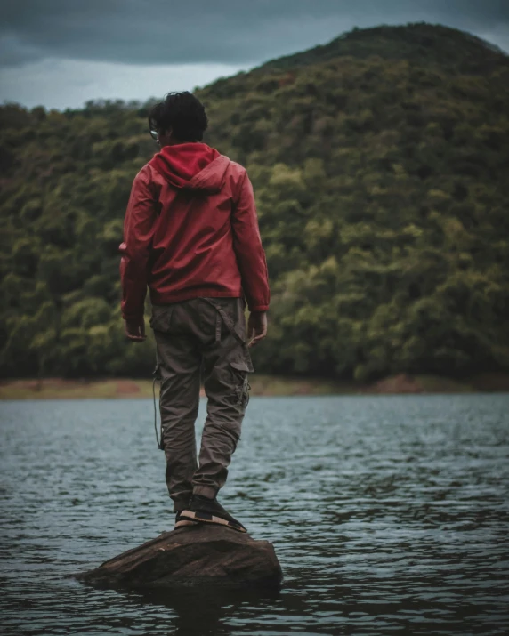 a person in a red jacket standing on rocks in the water