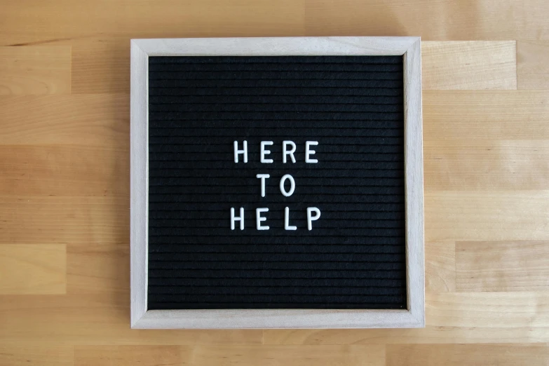 a wooden table holding a piece of black fabric with the words here to help written on it