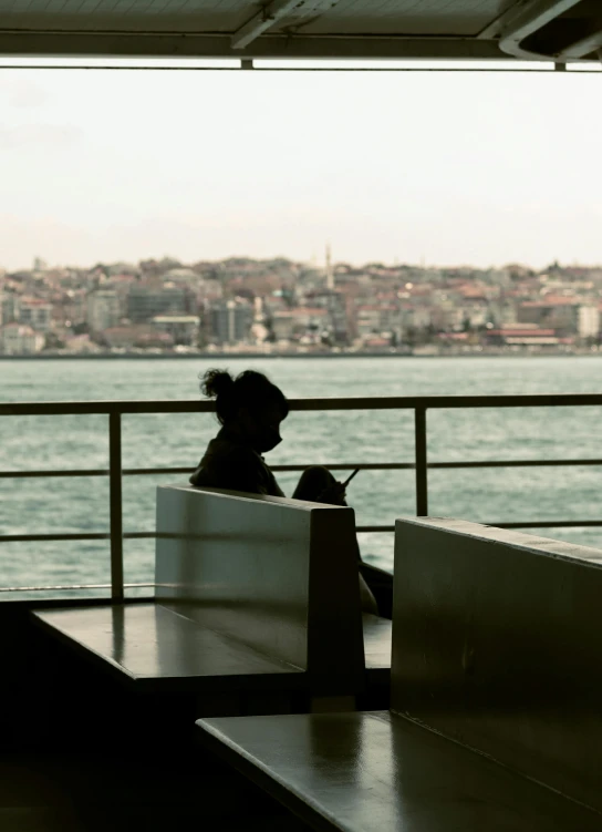 there is a woman sitting on a bench by the water