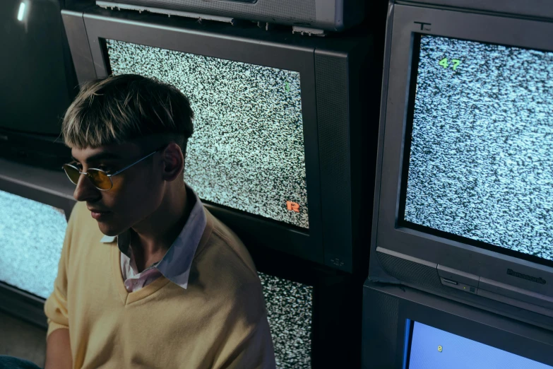 a man wearing sunglasses while looking at two televisions