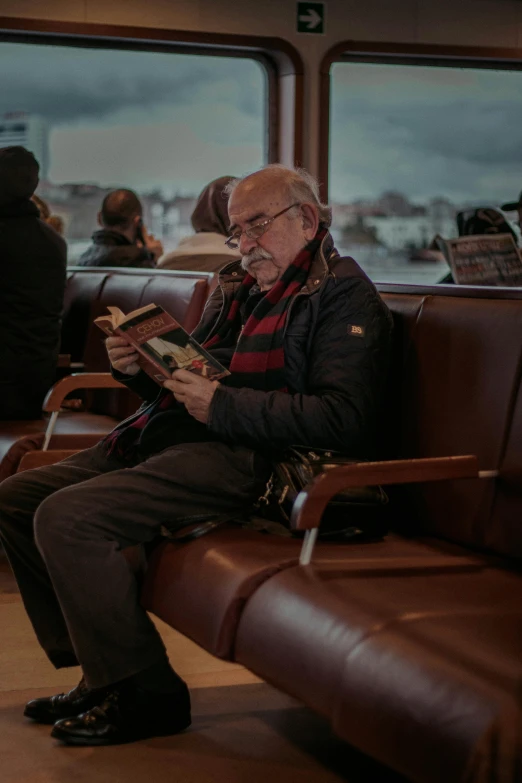 an elderly man sitting on a passenger train reading a book