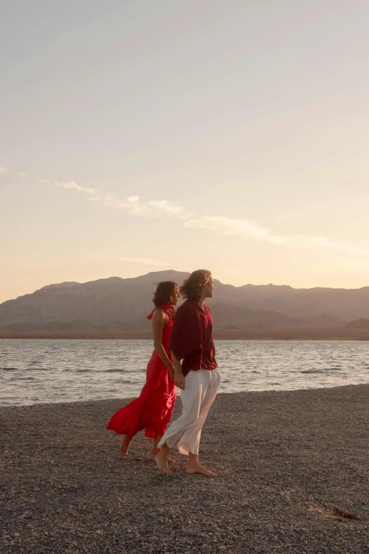 two people walking on the beach, one with a red shirt