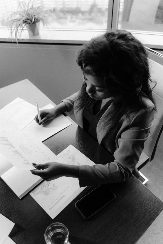 a woman sitting at a table writing on some papers