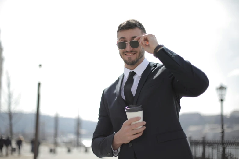 man in suit and sunglasses, holding a cup and looking to the side