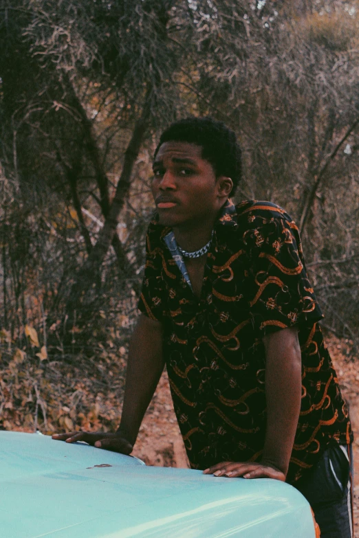 a man leaning on a car in the woods