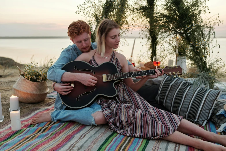 a man and woman sit on the beach with their guitar