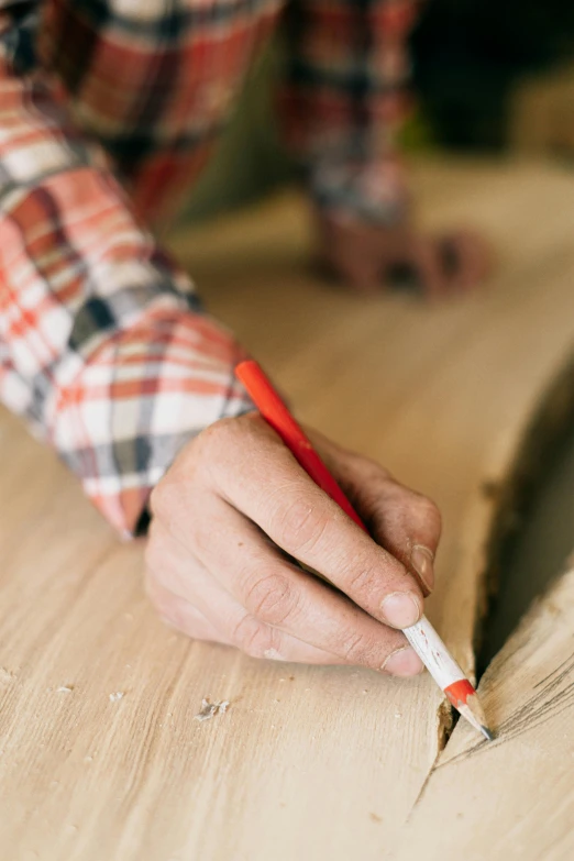 person with pencil in hand using a piece of wood