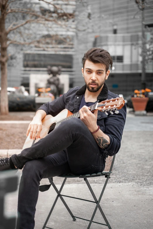 a man with beard sitting on a chair with a guitar