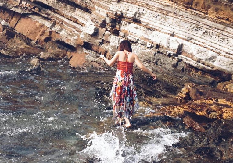 a woman wearing a floral dress standing in a rocky stream