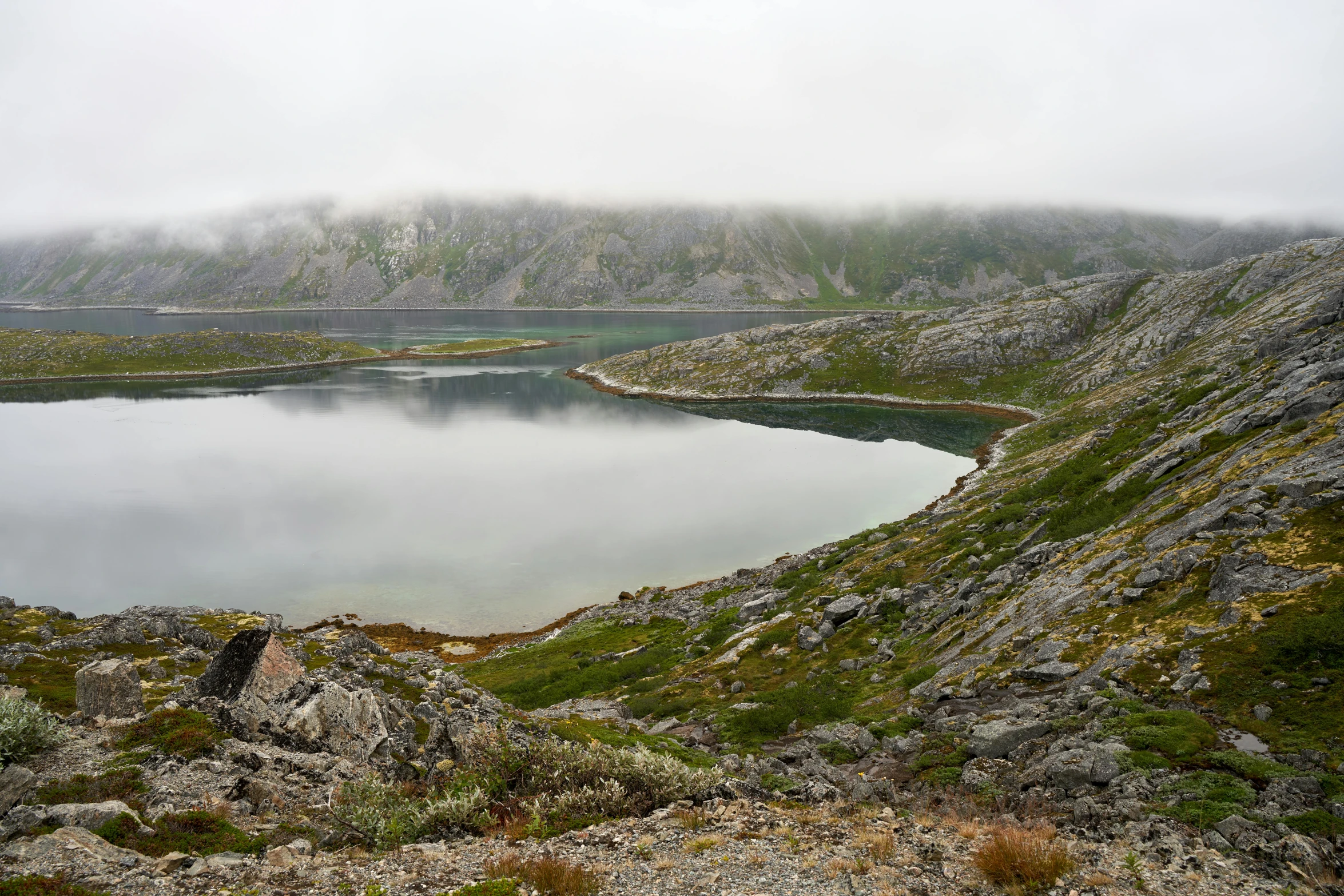 a lake on the side of a mountain covered in fog