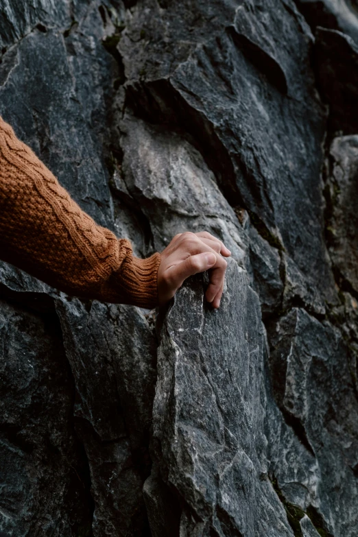 a person holding onto a rock by a mountain