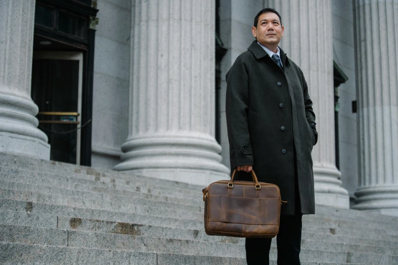 a man in a black coat with a brown bag stands near steps