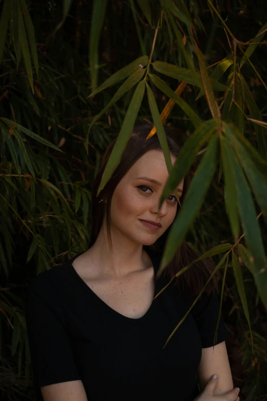 a woman standing in front of green plants, looking at the camera