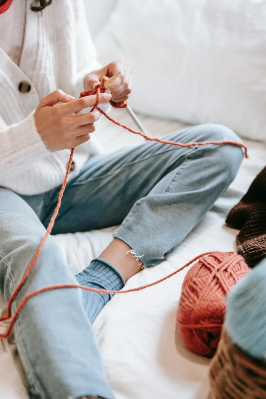 a girl in white sweater knitting a ball of yarn