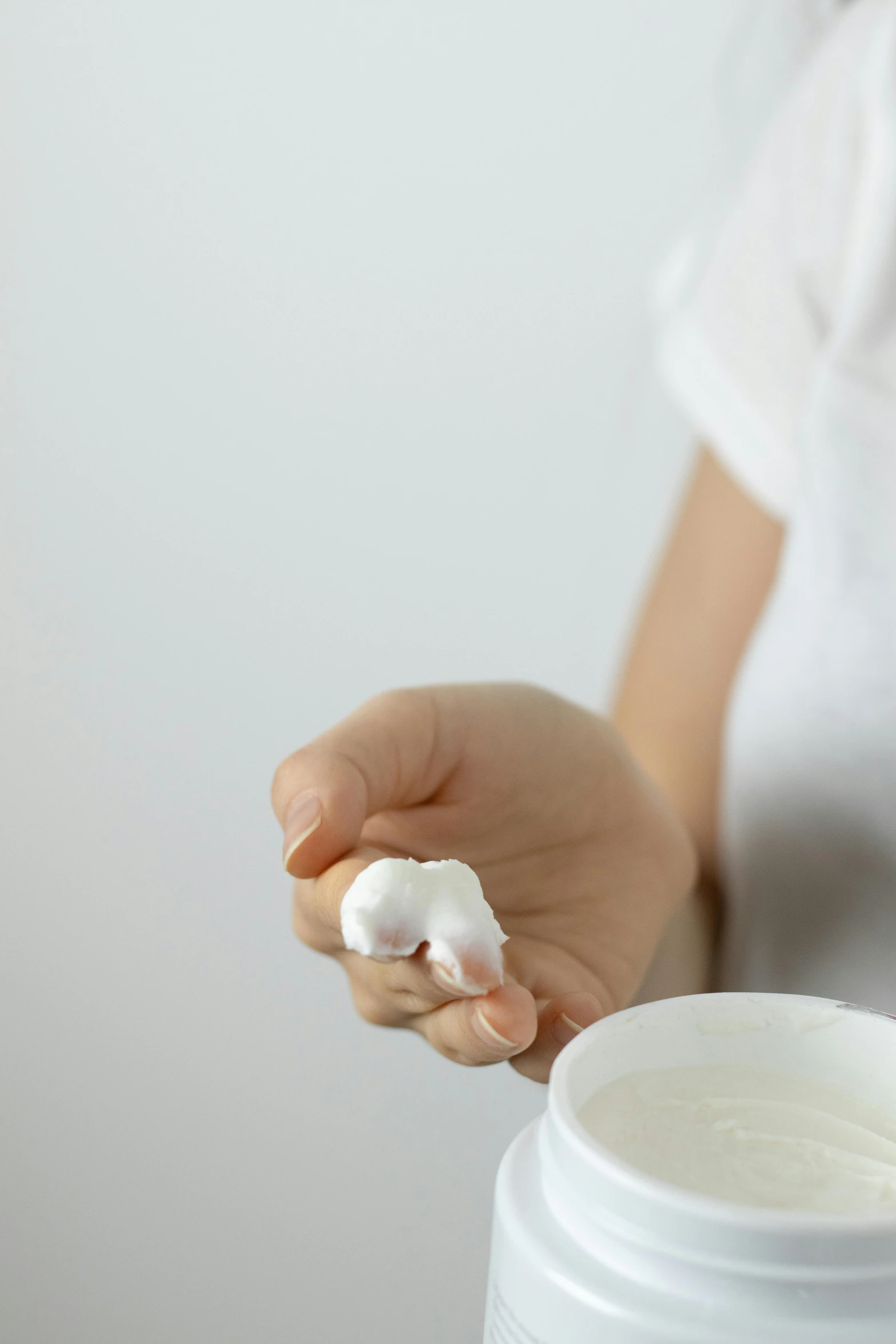 a person holding a container with some white cream on it