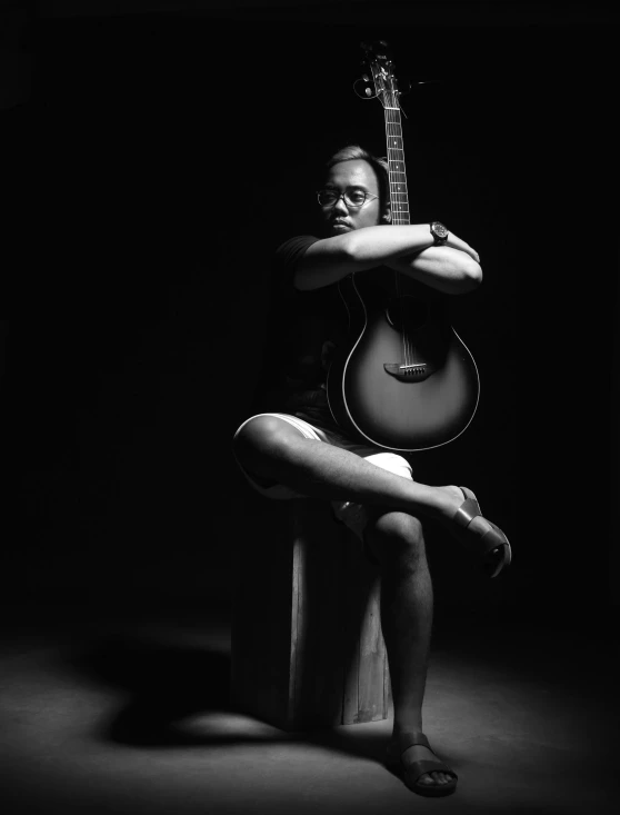 woman seated on stool playing a guitar against black background