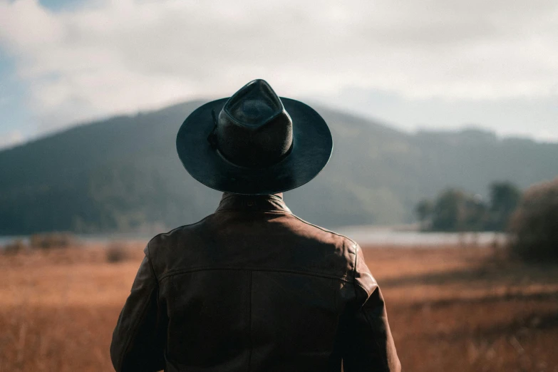 the back view of a man in a cowboy hat looking out at a field