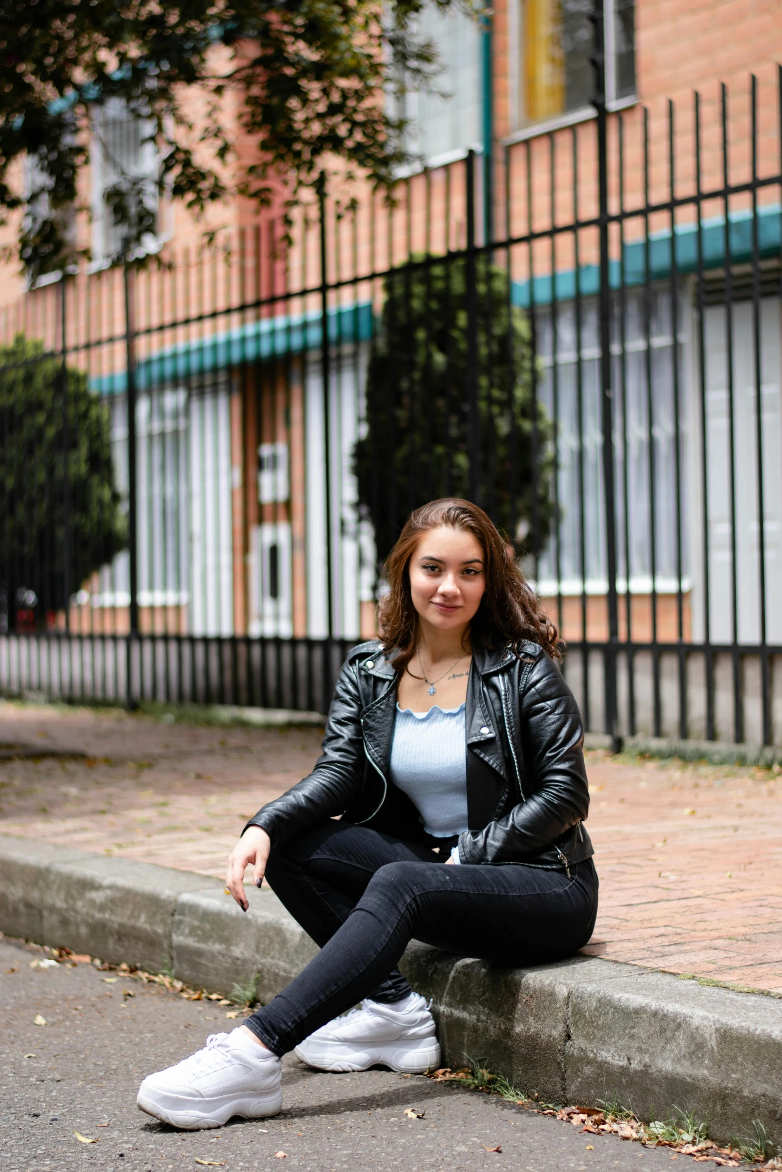 the girl is wearing a black leather jacket and white sneakers