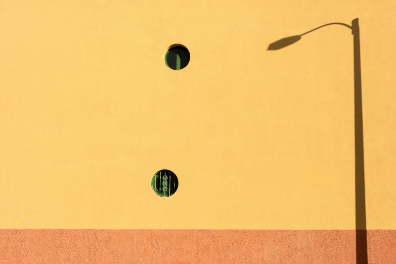 a yellow wall with three round holes and a light pole