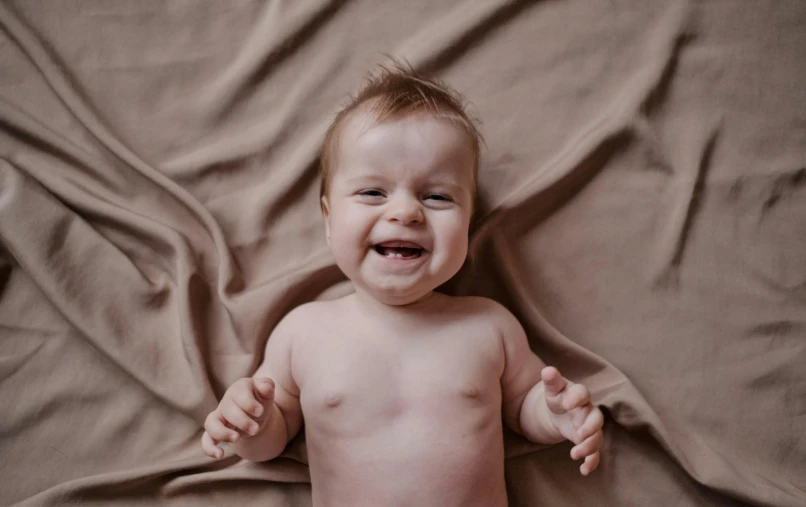 a crying baby on a blanket has two hands out