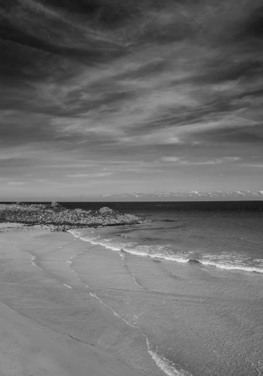 a beach scene with a cloudy sky, water and clouds