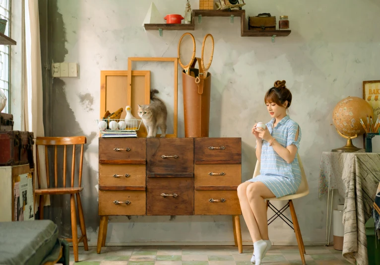 the woman is sitting in front of a dresser and drinking from a cup