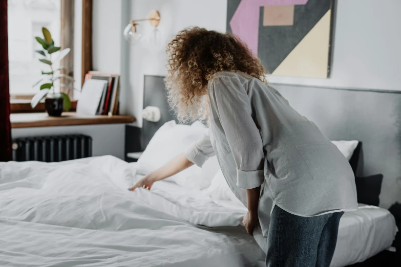 woman reaching for comforter on a white bed