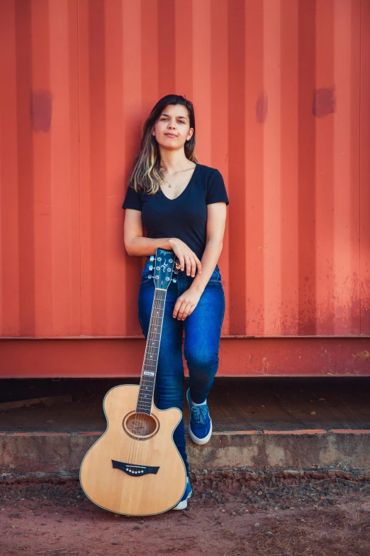 a girl poses with her guitar against a wall